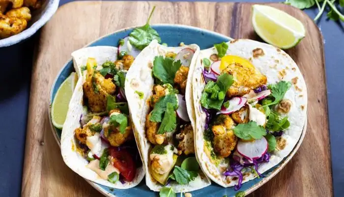 Close-up of roasted cauliflower tacos topped with vibrant red cabbage slaw and lime.
