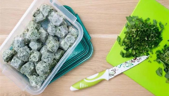 Freshly chopped green herbs frozen into an ice cube tray with olive oil, ready for storage.