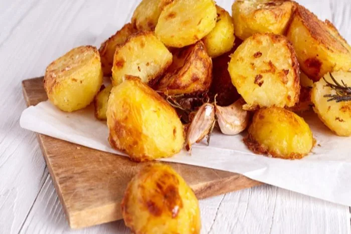 A close-up of crispy, seasoned roast potatoes on a baking tray, highlighting their golden, crunchy exterior.