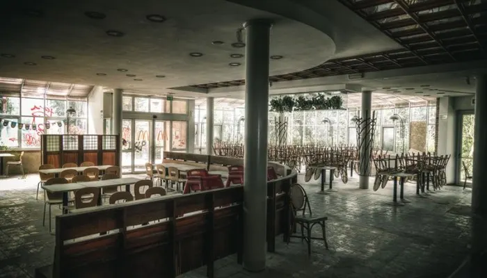 Exterior view of the abandoned Riccione McDonald's with graffiti and overgrown vegetation showing nature reclaiming the space.