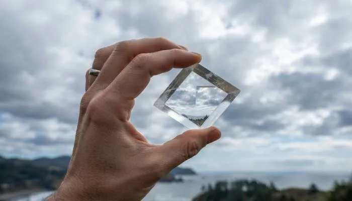 A transparent piece of Iceland spar crystal held up to demonstrate light polarization against a cloudy sky.